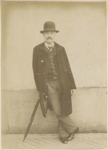 Portrait of a standing French man with a long coat, a hat and an umbrella