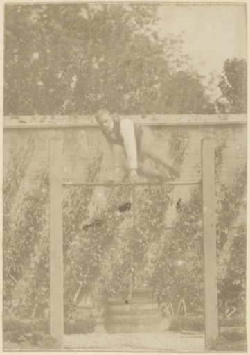 French man jumping over a stick in a garden
