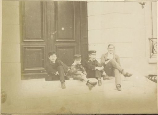 Group portrait of four seated French boys making faces in front of a door