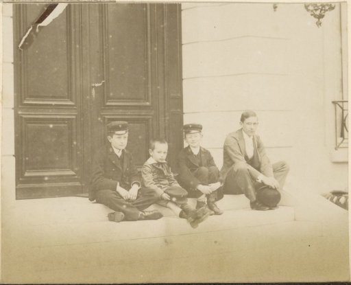 Group portrait of four seated French boys in front of a door