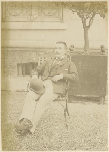 Portrait of a French man with a bowler hat in his hand, seated in a garden