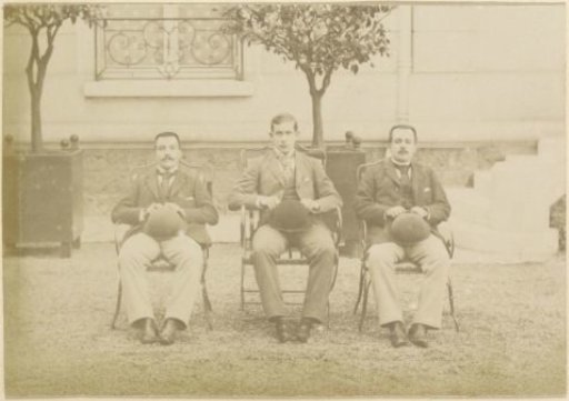 Group portrait of three French men with a bowler hat in their hand, seated in a garden