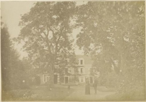 View of a house in France with a man, a woman and a dog in a garden in the foreground