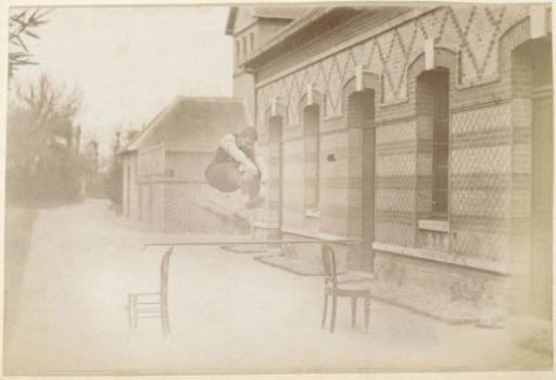French man jumping over a stick between two chairs in a yard