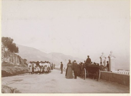 Road with a group of men in costumes and a party with a carriage, probably on the coast of Southern France