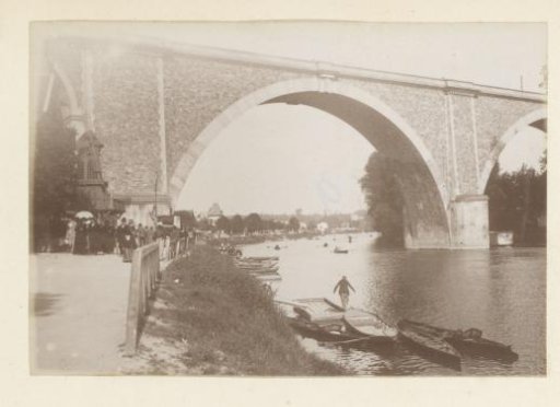 River view with stone bridge, rowing boats, windmill and walkers in France