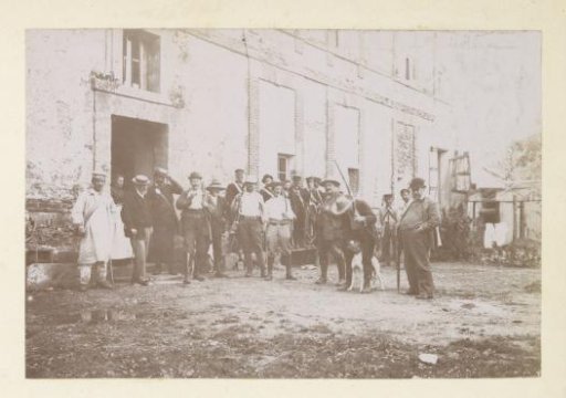 Group portrait of a hunting party in front of a house with bricked-up windows in France