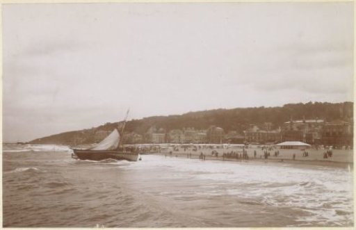 View of (probably) the French coast with sailing boat, houses and people on the beach
