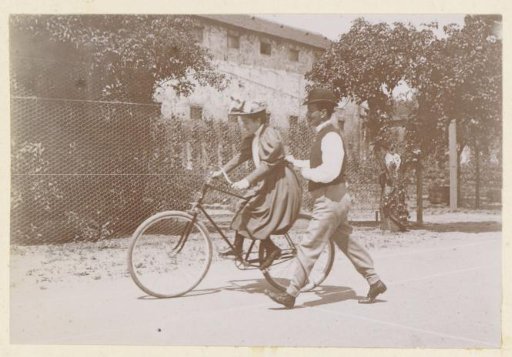 Man teaching a woman to cycle, probably in France