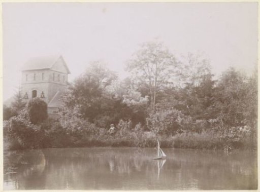 Boy playing with a toy sailboat, probably on a waterway in France