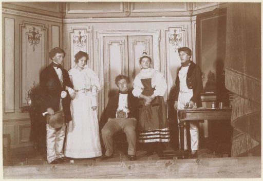 Group portrait of a company in historical costumes on a stage, probably French amateur actors