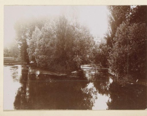 Waterway bordered by trees in France with a man on a bridge