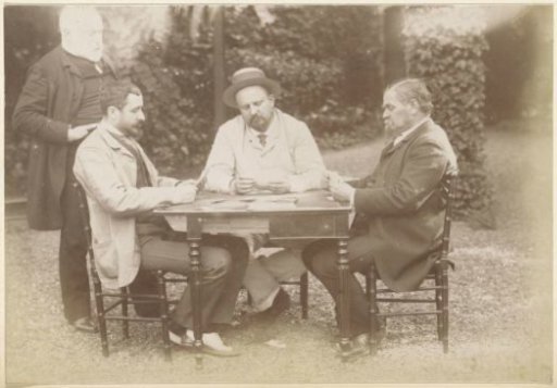 Three men playing cards at a table in a garden in France, one man watching