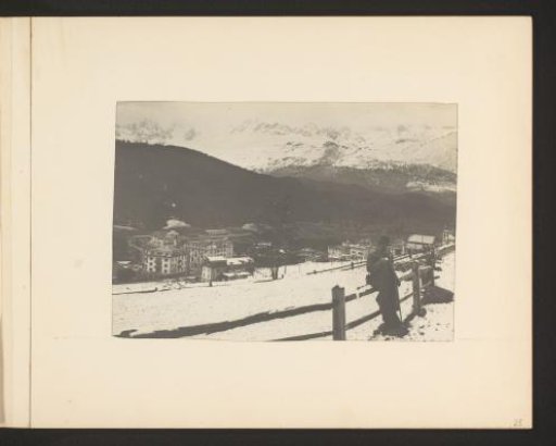 View of a village in a valley, a man with a hat leaning against a fence on the right