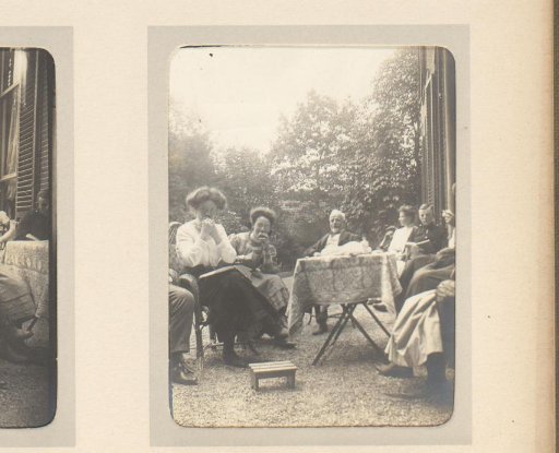 Company sitting outdoors around a table, two women biting into a fruit