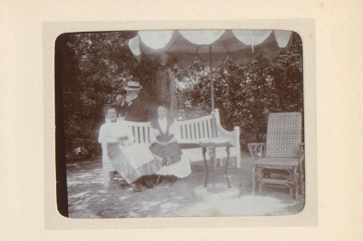 Group portrait of two women on a garden bench and a man standing behind them