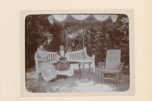 Group portrait of two women on a garden bench and a man standing behind them