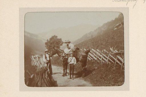 Woman on horseback, man and boy beside her, on a mountain path