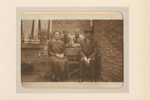 Group portrait of a man, woman, and two boys on a bench in front of a house