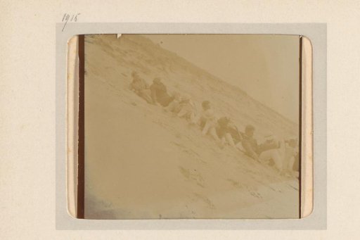 Group forming a train by sitting one behind another on a slope, possibly on the beach