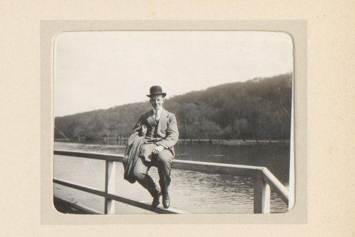 Portrait of a man with a round hat, sitting on a wooden fence along a river
