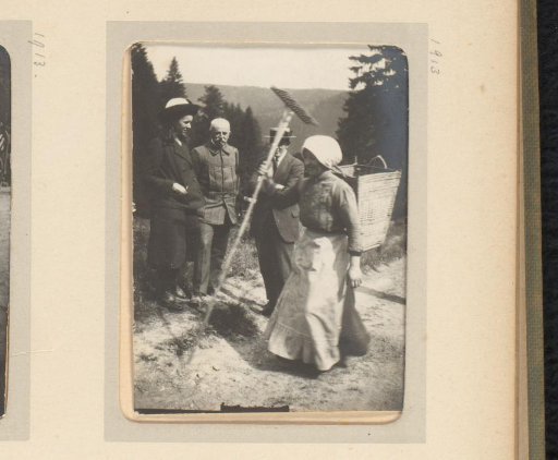 Woman with a basket on her back and a rake walking along a path; a woman and two men stand by the side