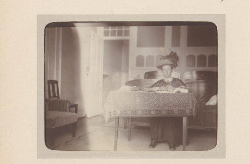 Portrait of a woman with a hat sitting behind a table in a bedroom