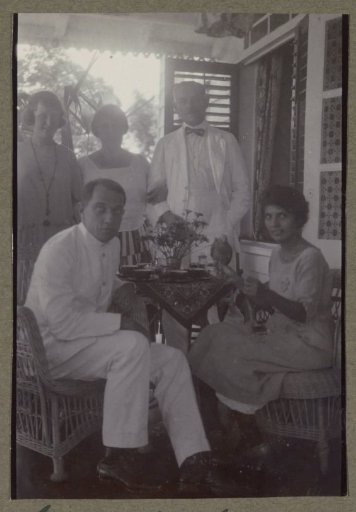Group including members of the Terlaak family on a veranda during a bamimeal, possibly in Suriname