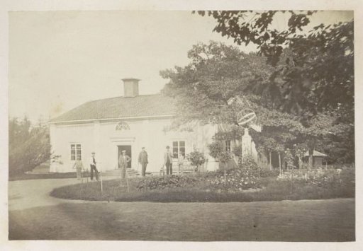 Men and Boys in a Flower Bed with a Sundial Near a House