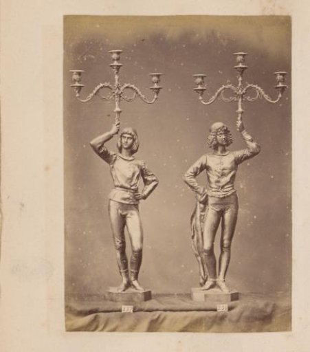 Two metal candlesticks with three arms, supported by a young man