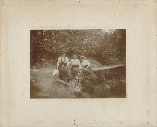 Three women sitting in a wood by a path