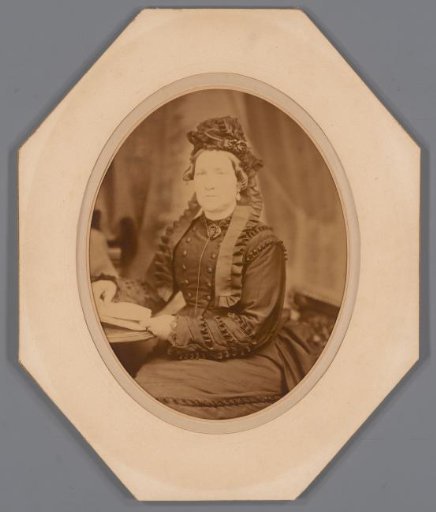 Portrait of an unknown seated woman at a table with a cap with ribbons