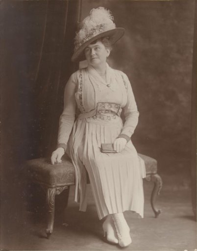 Studio portrait of a seated woman with hat and portfolio
