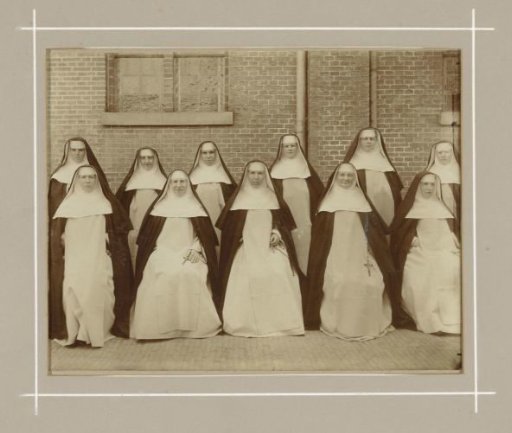 Group portrait of nuns in front of a monastery wall, wearing black habits with white wimples