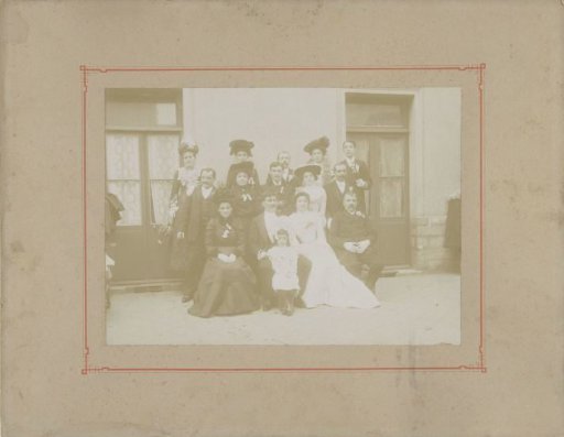 Group portrait of an unknown bride and groom with family in front of a house