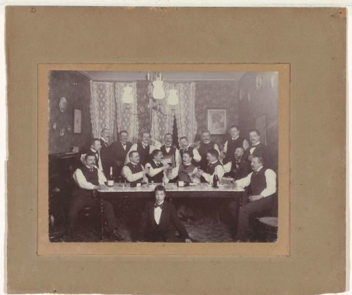Group portrait of men in suits, seated in a room with bottles, cigars and a painting