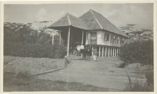 Portrait of an unknown married couple in a carriage with a servant in front of a house in the Dutch East Indies