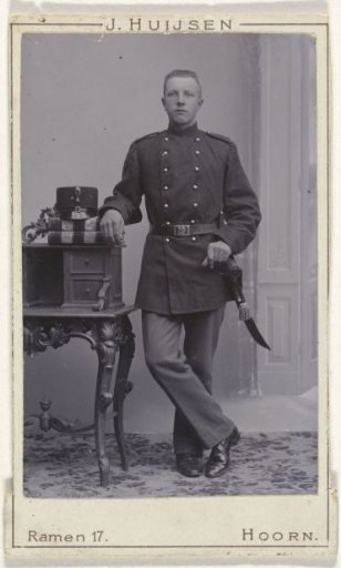 Studio portrait of a man in uniform by a sideboard