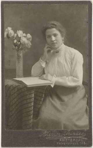 Studio portrait of a young lady in a high-collared dress reading at a table
