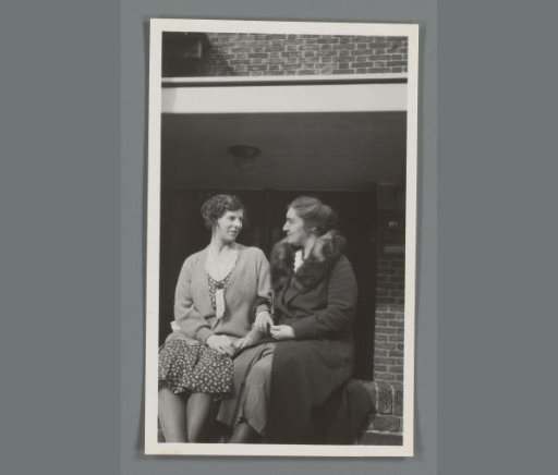 Two women sitting in front of a house