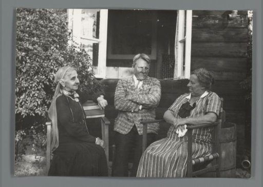 Two women and a man sitting in front of a house