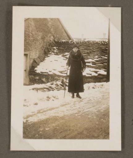 Woman with walking stick, standing in front of a house at Pezzolo