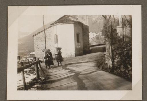 Three women with a basket on their backs in front of the church of Campestro, Switzerland