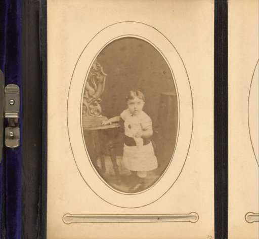 Portrait of a Toddler in a White Dress, Standing by a Table
