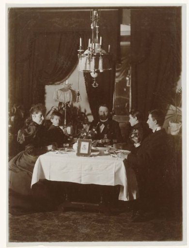 Family at table, with a framed photograph on the table