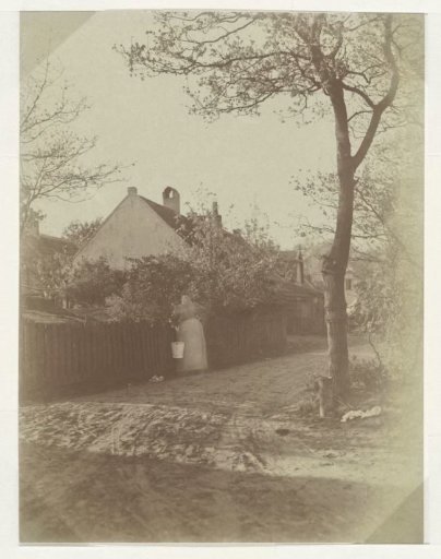 Woman with a bucket in her hand leaning against a fence on a sandy path