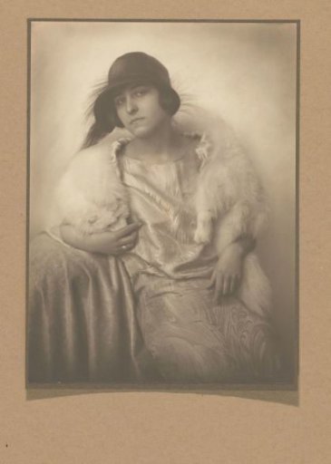 Portrait of Jo Merkelbach with a feathered hat and fur trim over a shiny dress