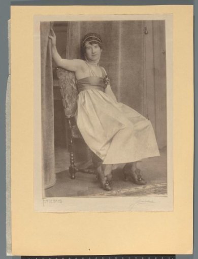 Woman in an evening dress with beads around her head seated on a chair