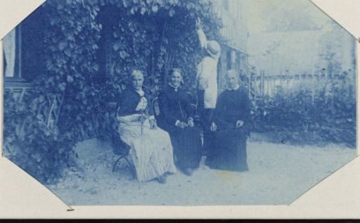 Group portrait of three unknown women and a man in front of a house