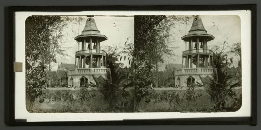 View of a bell tower with presumably a Buddhist temple in the background, Thailand